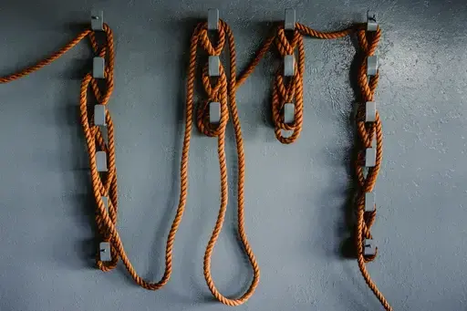A close shot of a large ship, with ropes wound intricately along a series of hooks on the side of the ship.